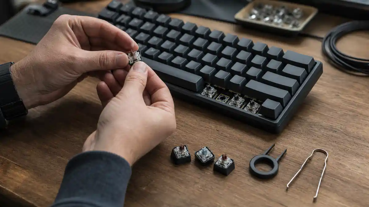 Hands inspect a mechanical switch beside a serviceable compact keyboard